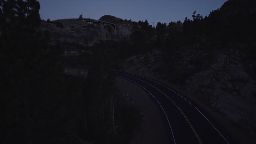Aerial view of a paved highway amid mountains with the silhouette of trees at dawn