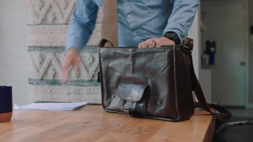 A closeup of a persons hands opening a darkcolored bag on a table storing documents inside