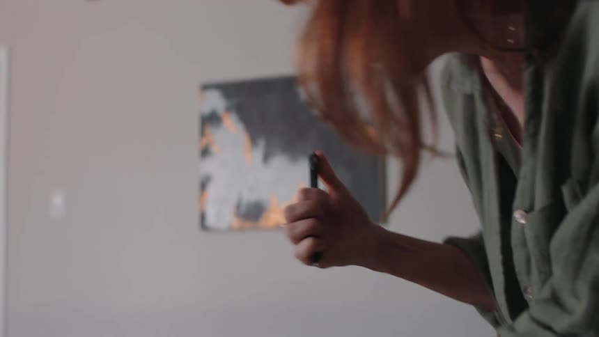 A red haired woman hustles over to a desk in a living room to write something on paper