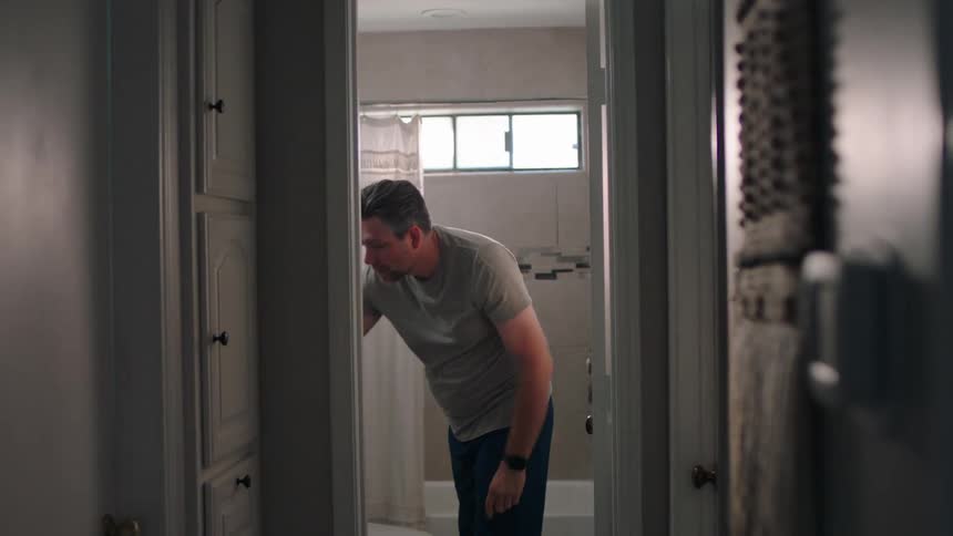 Man in the bathroom putting a watch on his wrist and walking out into the hallway of the house