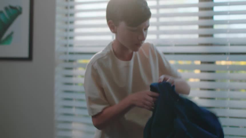 Boy in room next to bed looking for clothes on floor