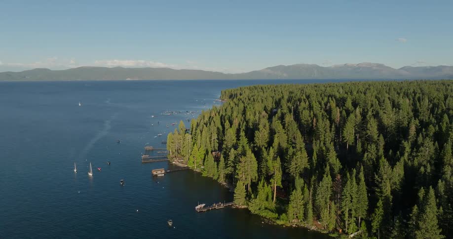 Aerial shot of yacht boats near a pier on a vast lake surrounded by mountains and forests