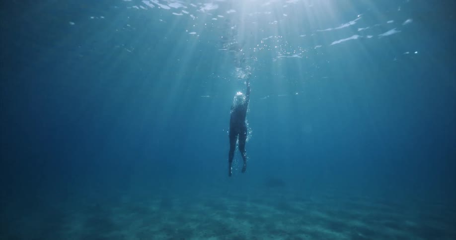 Person submerged in a mountain lake with clear waters and reflection of sunlight rising towards the surface