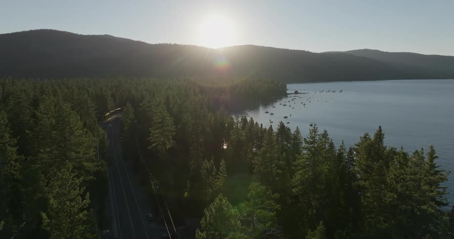Aerial veiw of a sunset over a forested area next to a calm lake with scattered boats on the water