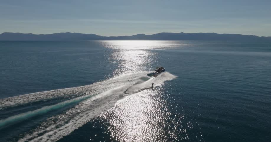 A person water skiing behind a boat on a calm reflective sea with mountains in the background