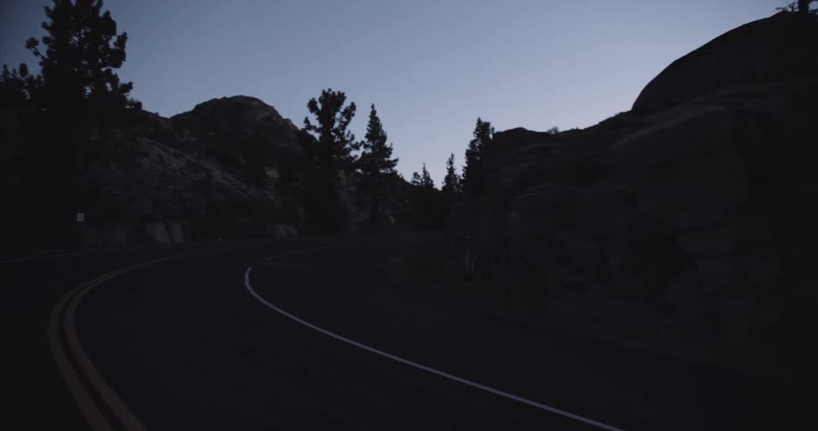 Asphalt road surrounded by a silhouette of mountains at dawn