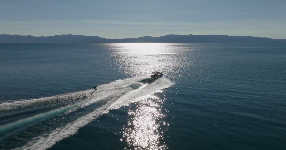 A speedboat creates a wake as it moves across a vast body of water behind the boat a person is wakeboarding