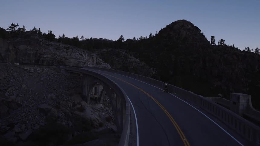 A bicyclist rides across a bridge in a mountainous area