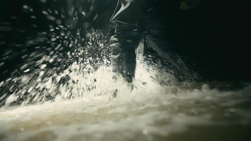 A person slow walks through ankle deep water which causes it to splash