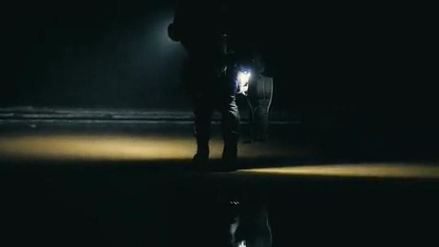 A person is walking on a beach at night using a flashlight and going to the sea