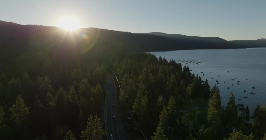 Aerial panorama of a highway surrounded by vegetation and the edge of a lake with boats and the sunset on the horizon