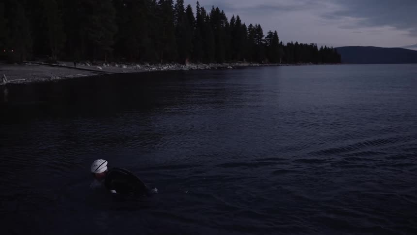 A person in a wetsuit and a diving cap is coming out of the water and heading towards the shore