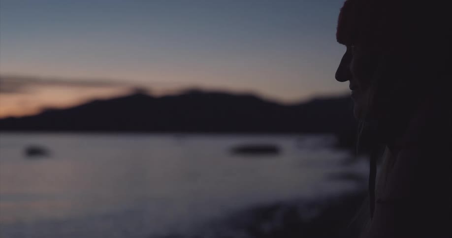 A woman watches a mountain lake at sunrise