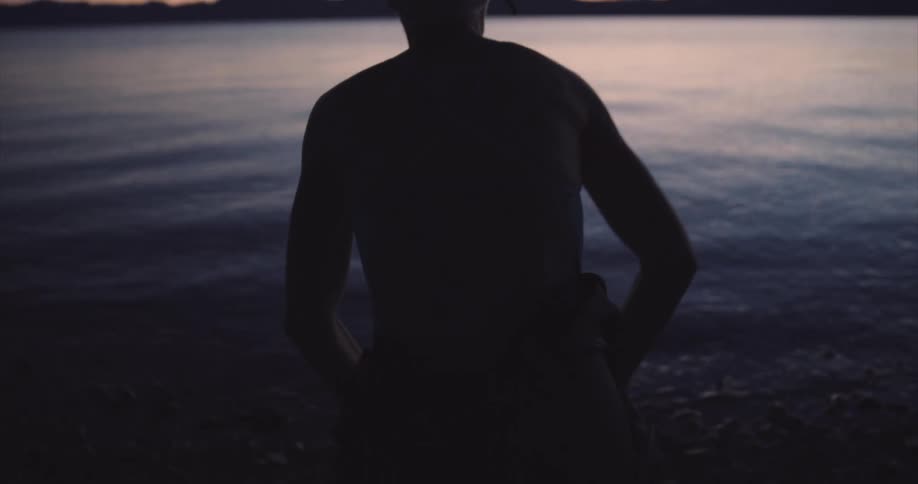 View of a person from behind preparing to swim in front of a lake at dawn