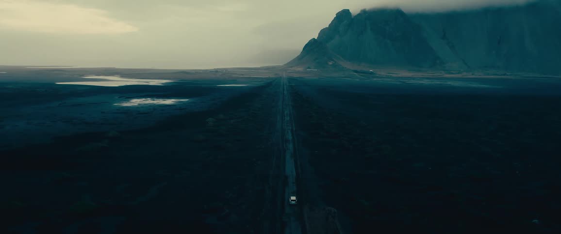 A vehicle drives down the long road towards a mountain