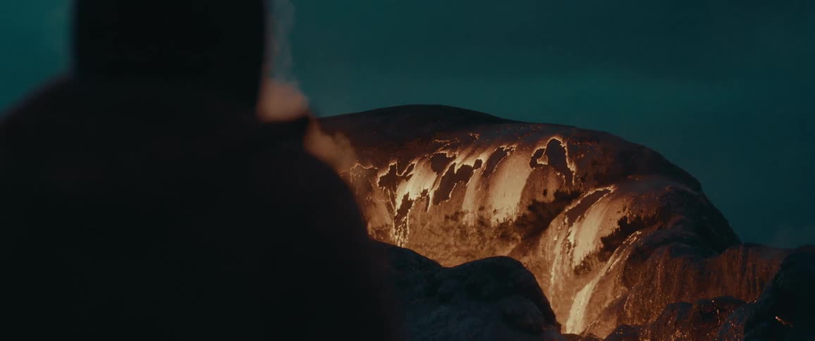 Silhouette of a person from behind watching lava falling from a volcano at night