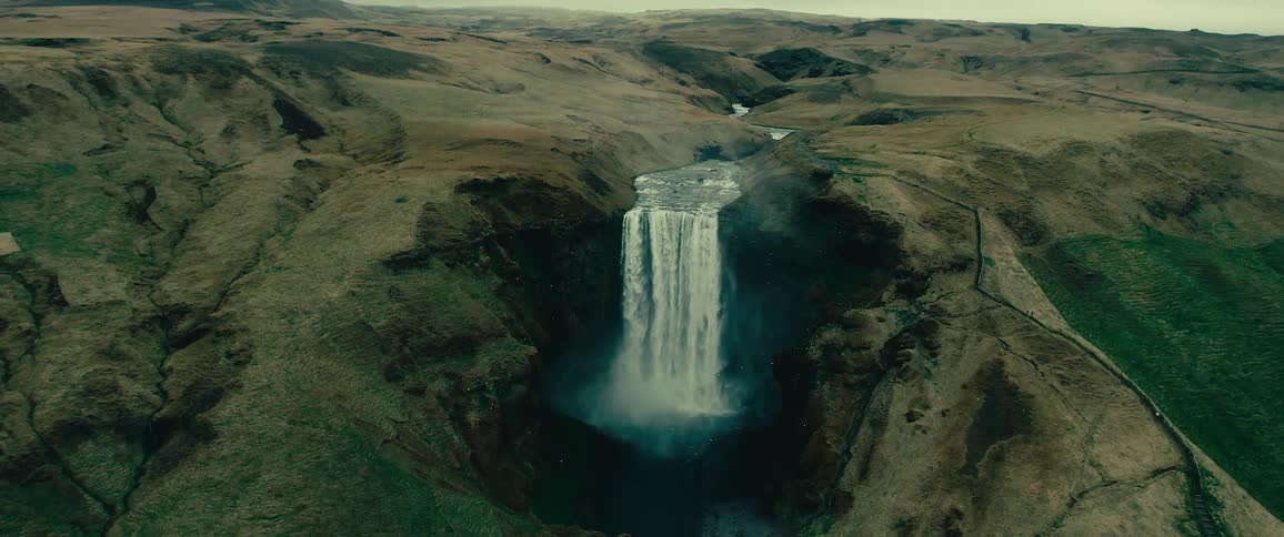 Aerial view of a large waterfall cascading down a rugged cliff in a sparse brownandgreen landscape