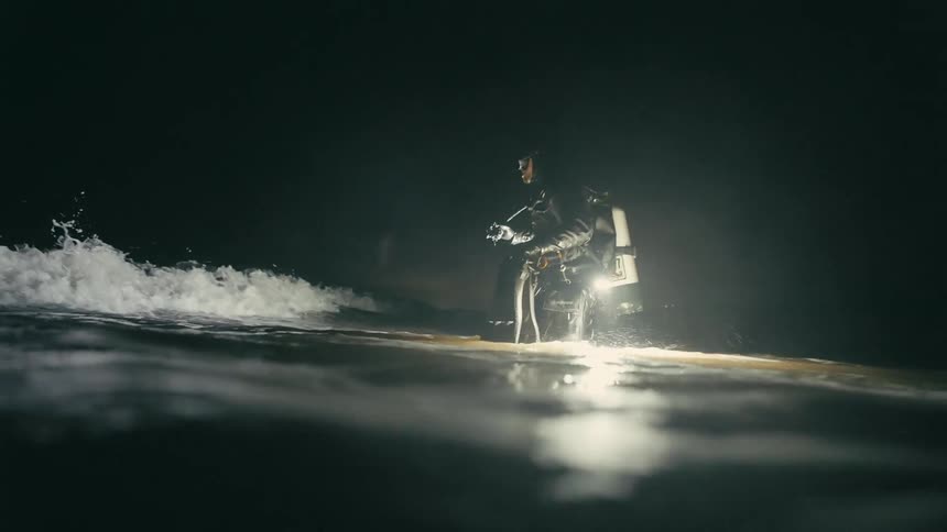 A white male diver wades into the ocean surf