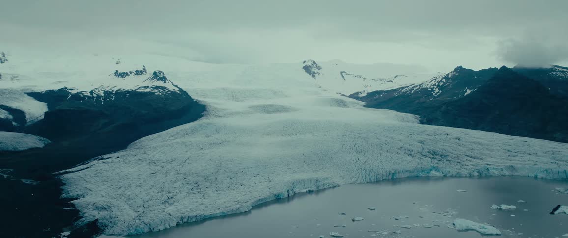 Aerial view of a vast glacier with a central ice formation leading into a meltwater lake