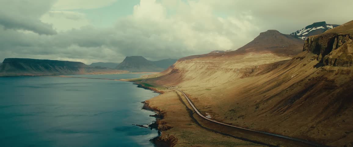 Aerial view of a highway next to mountains and the edge of a lake