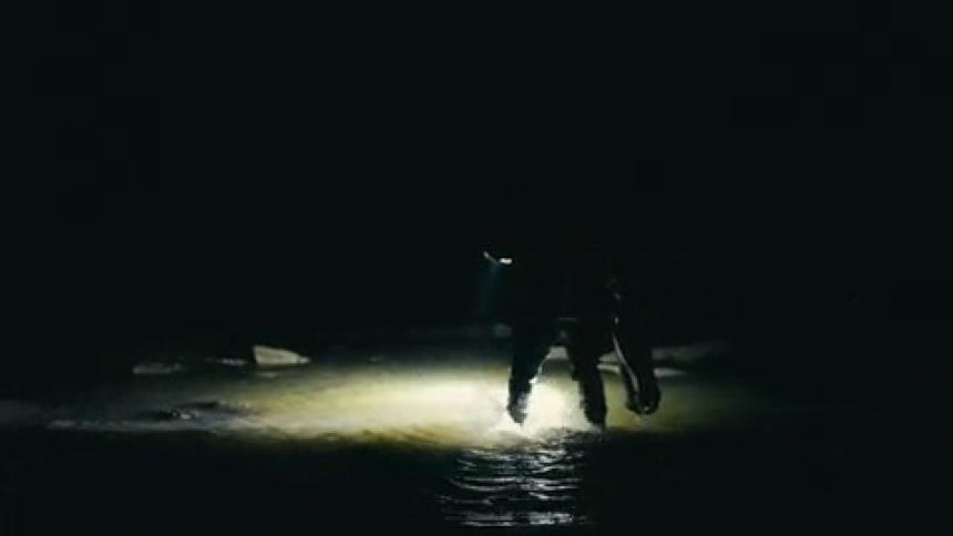 A person carrying gear walks from a beach into the ocean