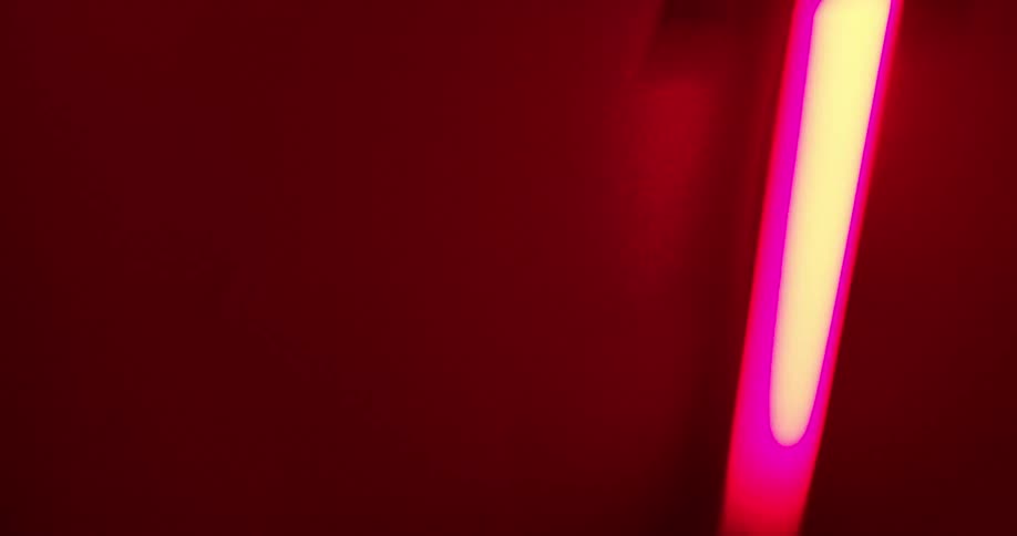 Blurry neon light closeup against a dark red background emitting a bright pink and white glow