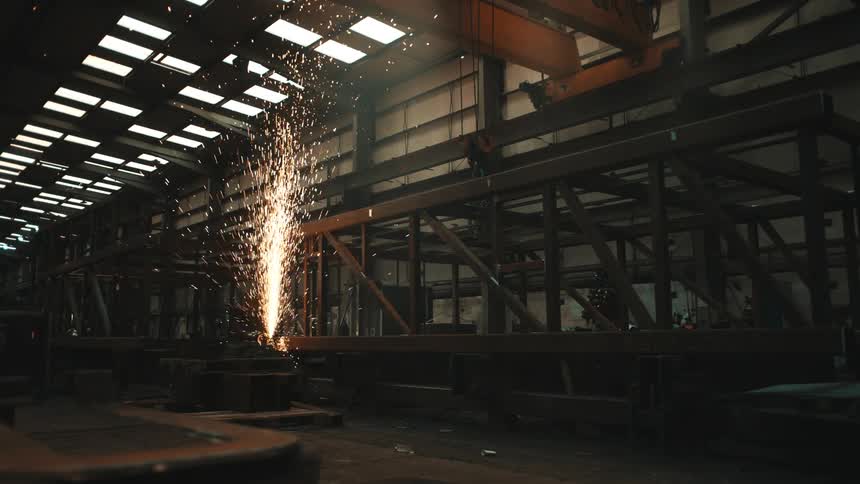 A welding scene in a spacious industrial workshop sparks flying as metal is being welded