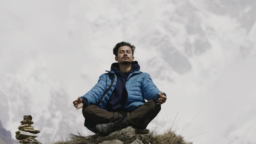 Man meditating on a rocky peak with snowy mountains in the background
