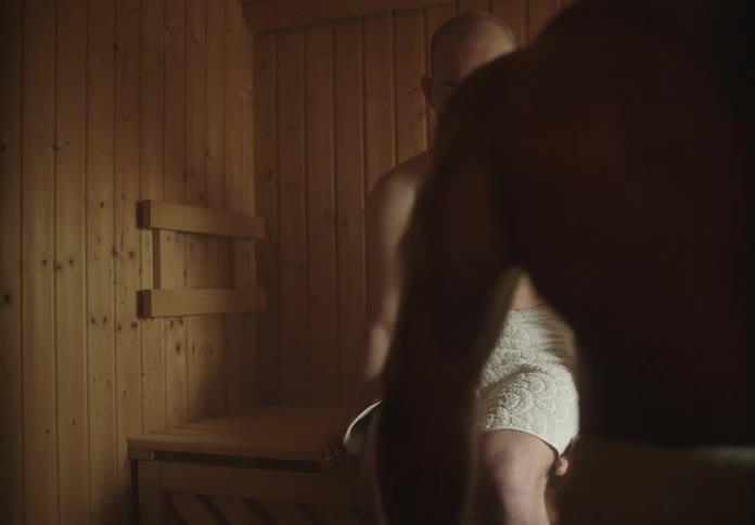 Two men in a sauna with one of them taking deep breaths