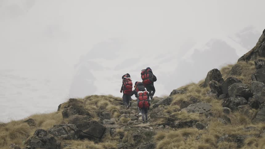 Group of people with backpacks hiking up a mountain on a foggy day