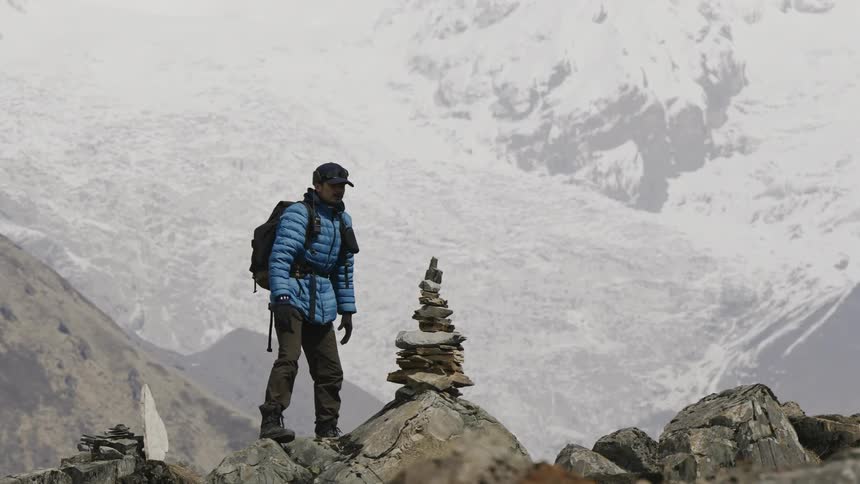 Man on a hill placing a stone on top of other balanced stones and snowy mountains in the background