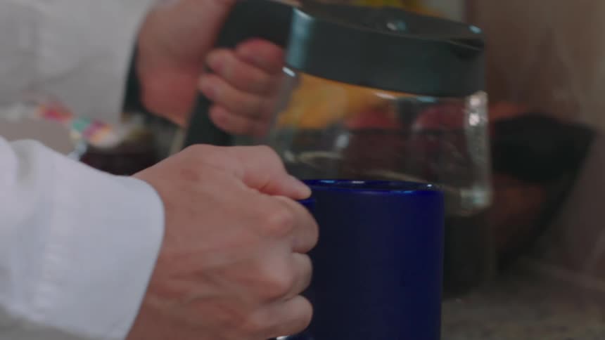 A man prepares his breakfast grabbing a mug and filling it with coffee then putting a toast on a plate and reaching for a flask of jam