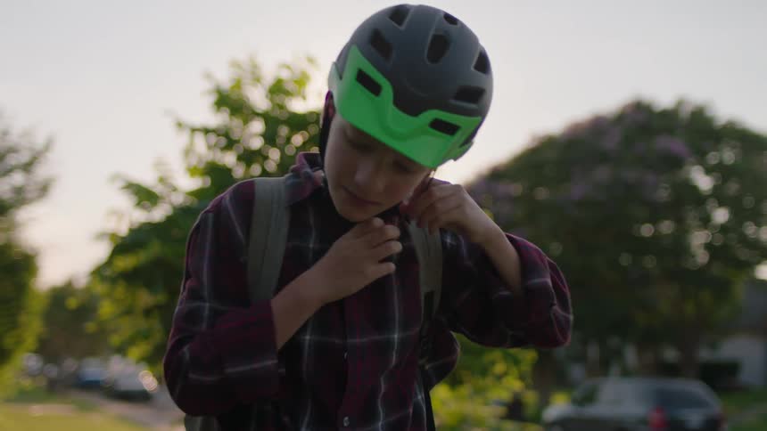 Young boy putting on helmet next to his bike
