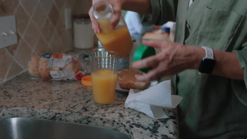 A woman pours orange juice into a glass on a kitchen counter