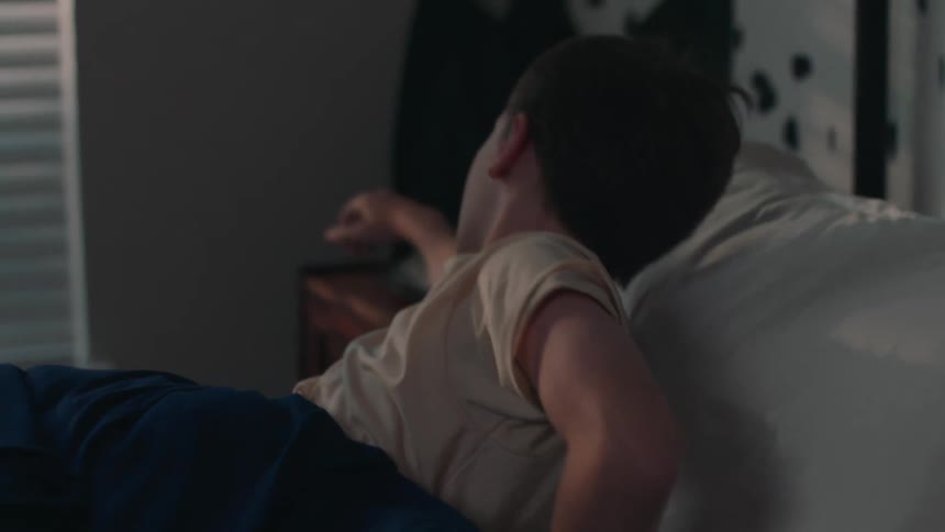 Boy being woken up by the alarm clock he turns it off and goes back to sleep