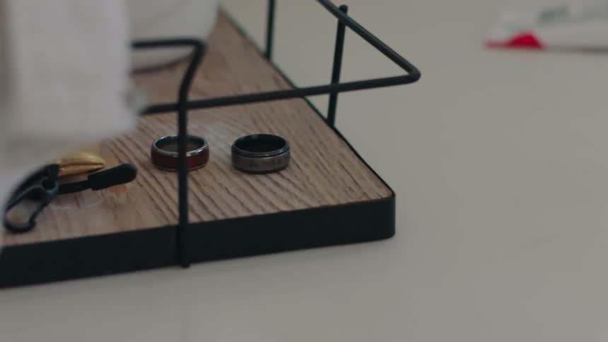 Hand picking up a smartwatch and a ring on top of a surface