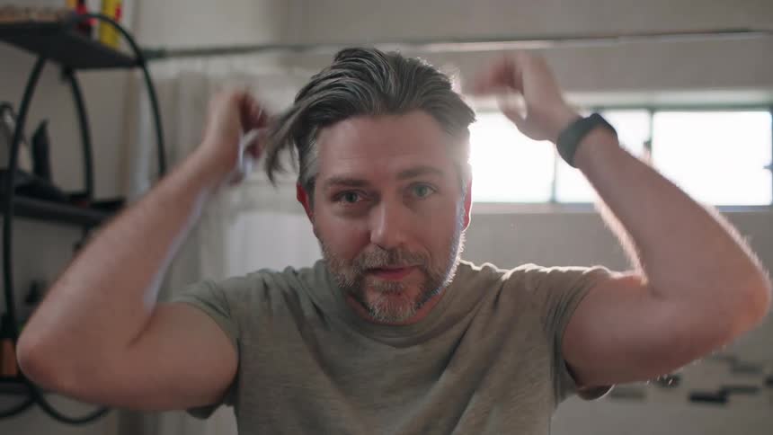 A man stands in the bathroom and runs his hands through his hair