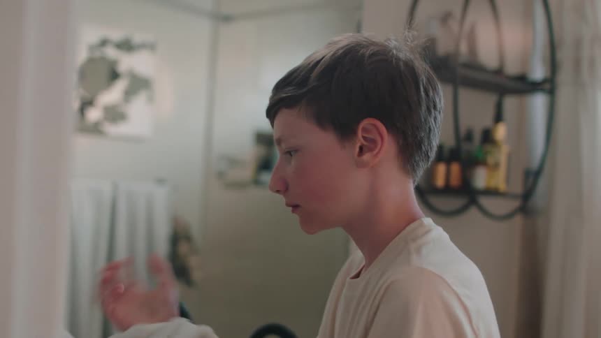 A boy wipes his face with a towel and exits the bathroom