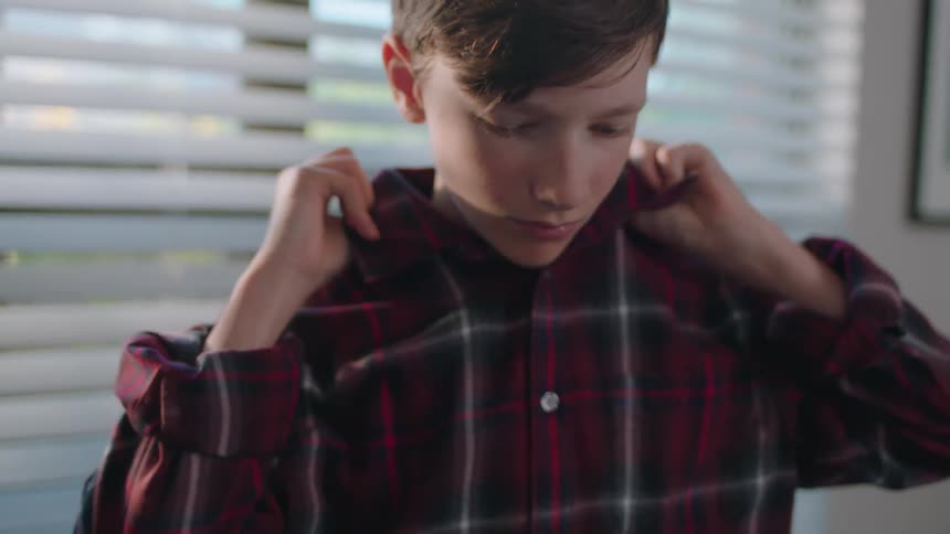 A boy is buttoning up his shirt