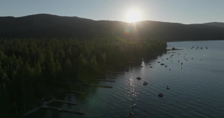 Aerial landscape of a lake with pier and yachts on the edge of a hilly forest with the sun on the horizon