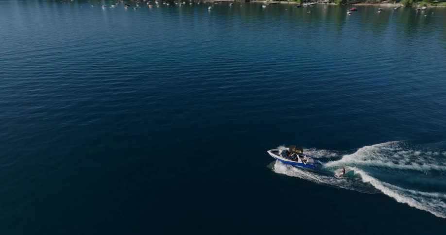 Aerial view of a speedboat slicing through blue water with a person wakeboarding behind