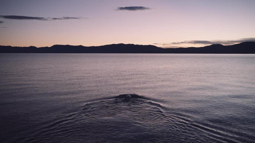 Swimmer wades into water and starts swimming toward mountains silhouetted against a red tinted sky at sunrise