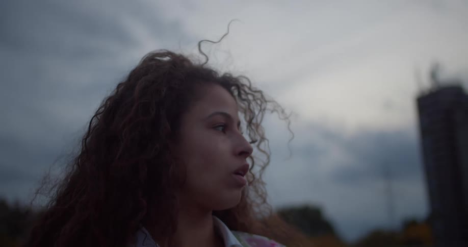 Portrait of a curlyhaired woman looking scared to the side in an outdoor setting