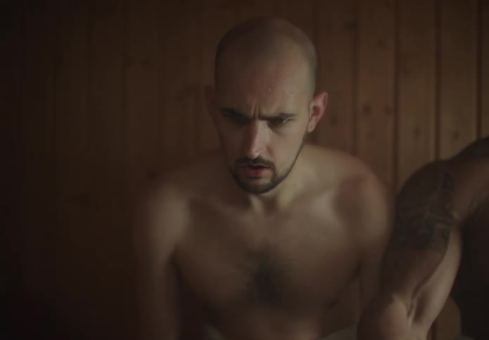 Man in a sauna scared as a muscular man sits next to him