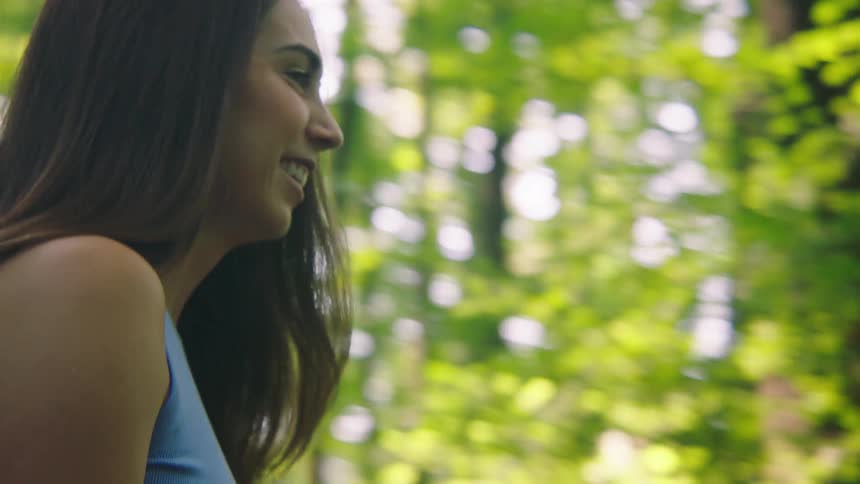 Happy woman walking on a trail surrounded by trees with two dogs on leashes