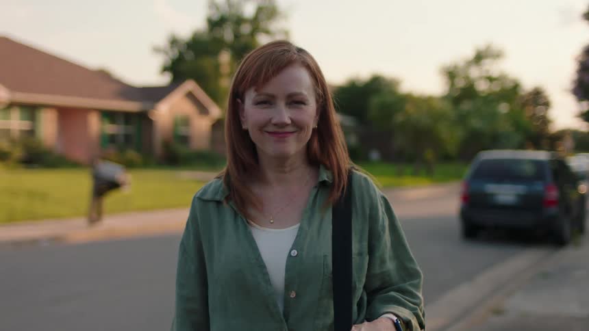 Portrait of a happy woman while standing on the sidewalk next to the street in a residential neighborhood