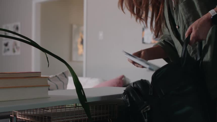 A woman fills a black briefcase with books and notebooks then leaves the room