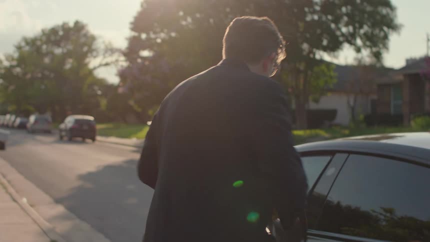 Man in a suit and carrying a backpack leaving his house and getting into a car