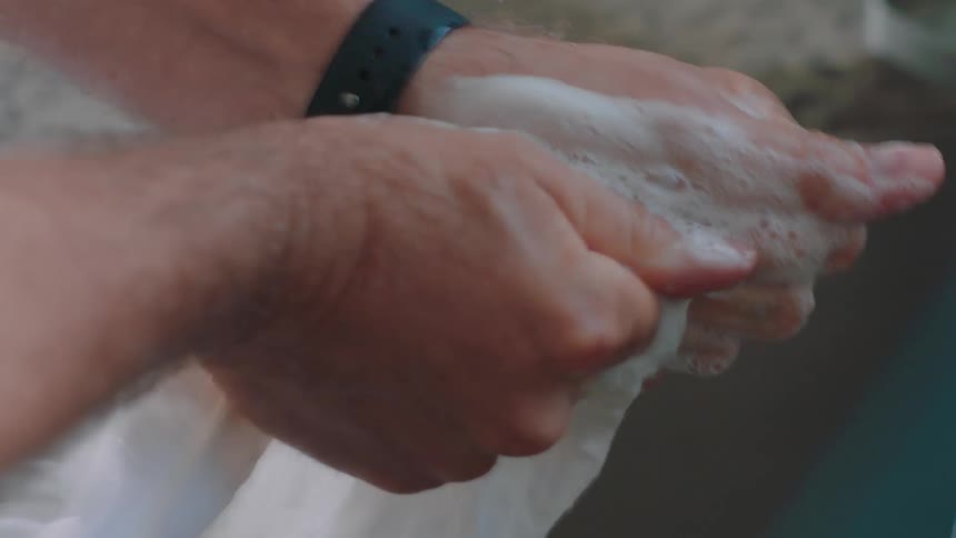 A closeup of a mans hands washing a white shirt at the kitchen sink in a home