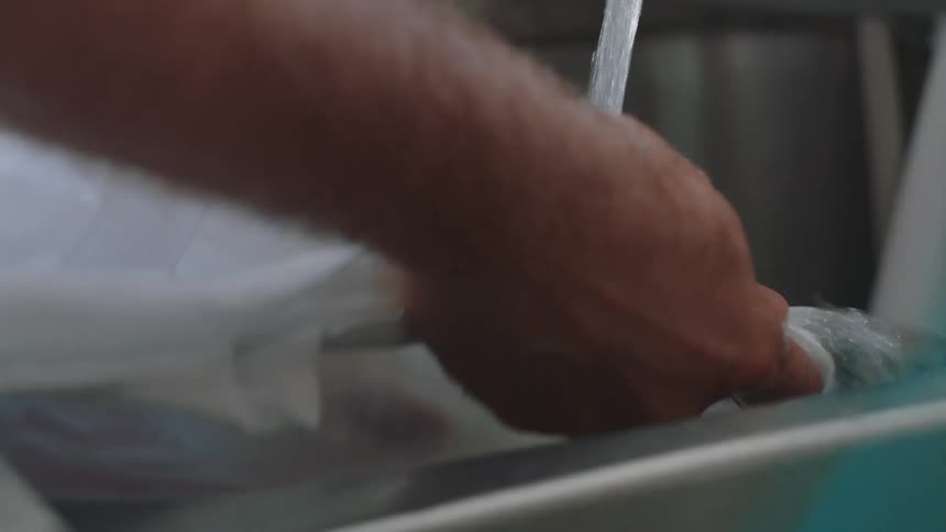 Close up of the hands of a person washing a shirt in the kitchen sink